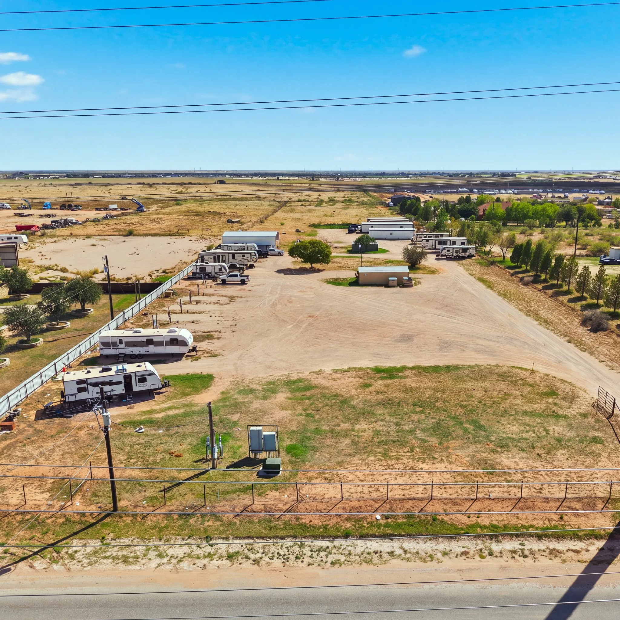 A1 RV Park from the air, above the county road: travel trailers along a white fence, a wide caliche lot, and the drive running back past a row of trees, with flat Permian Basin land to the horizon