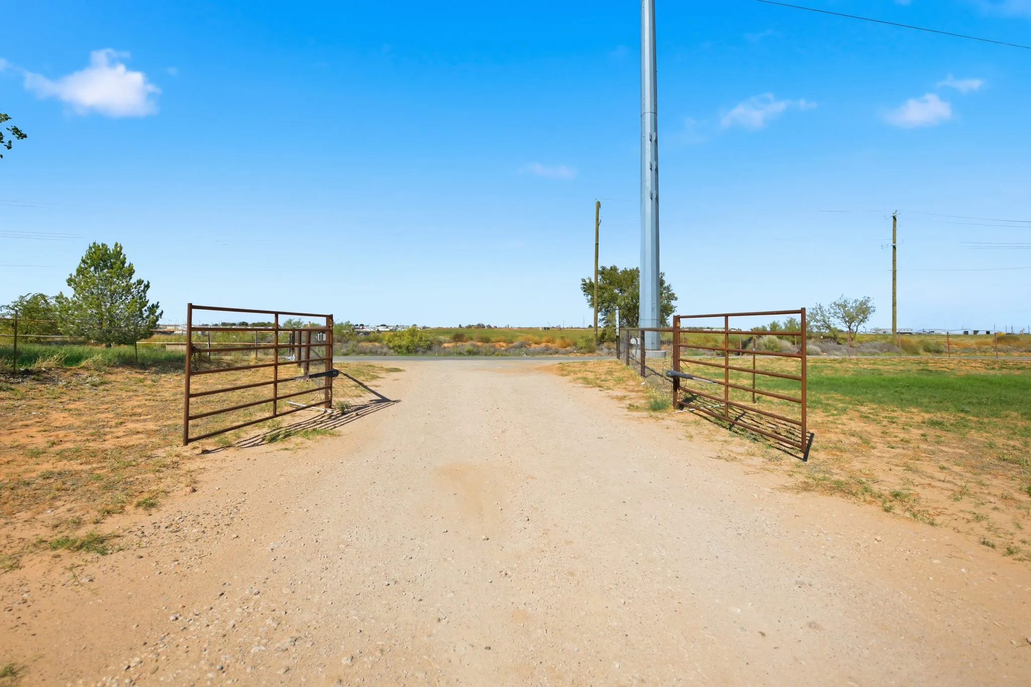 A pipe gate standing open across the caliche drive at A1 RV Park, under a clear West Texas sky
