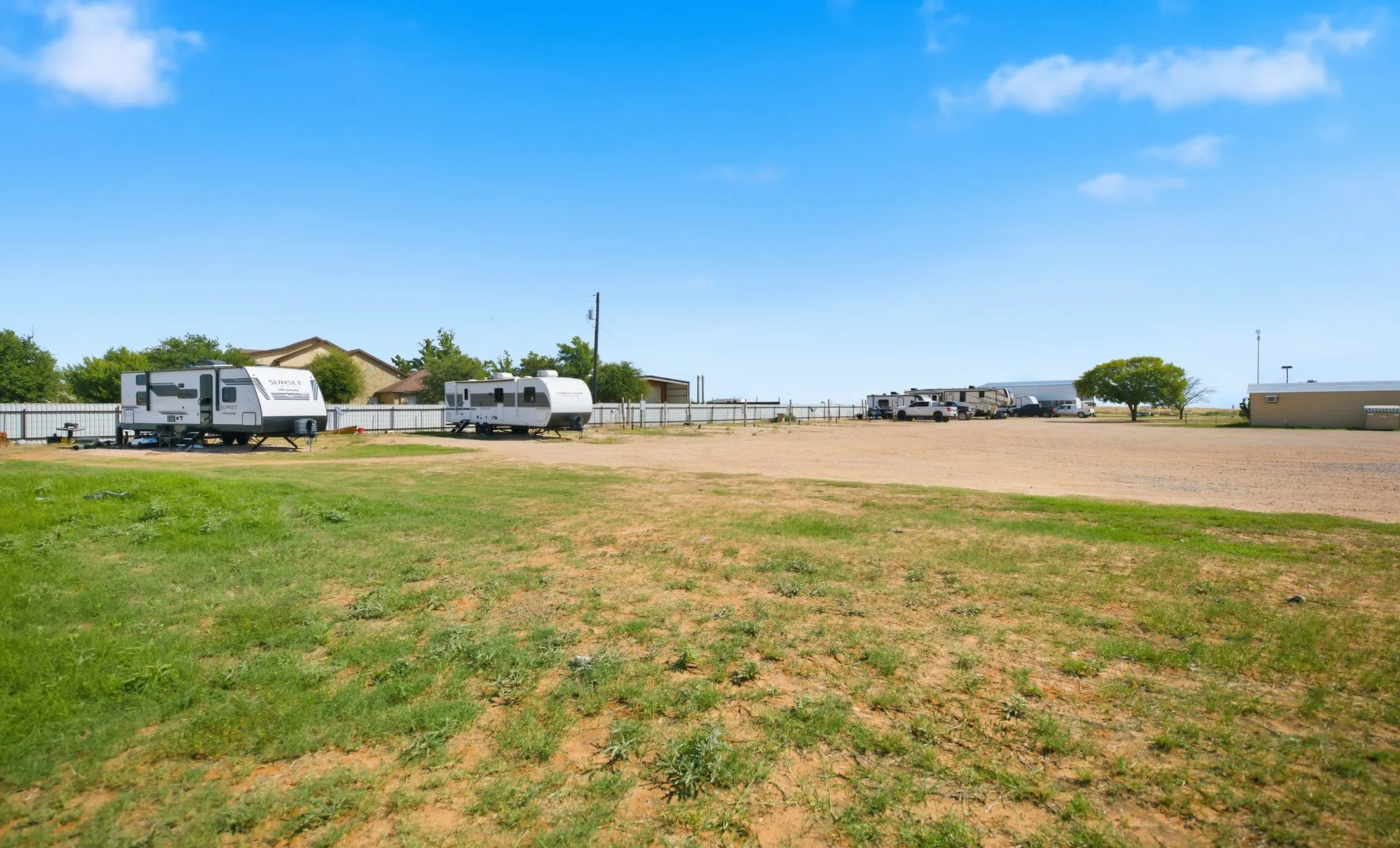 The grounds at A1 RV Park: travel trailers parked along a white metal fence, a wide gravel lot, and grass in the foreground